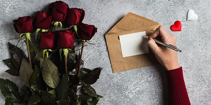 Romantic Things To Do On Valentine’s Day woman hand holding pen writing a love letter with greeting card