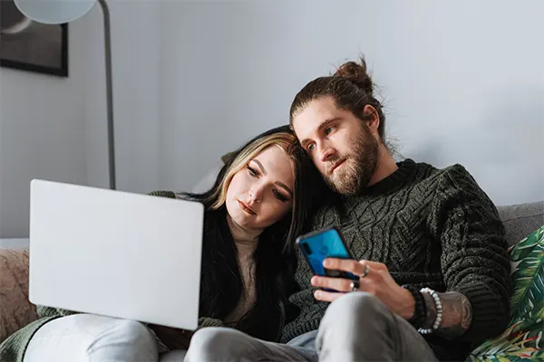 A couple sitting on a couch, engrossed in their laptop, enjoying Valentine's Day together.