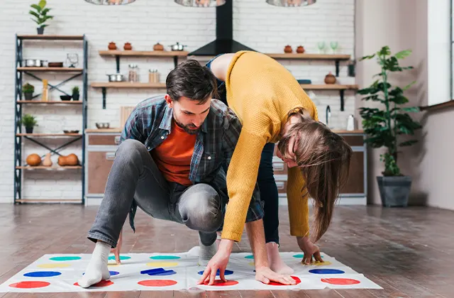 A young man playing Twister game with his wife at home.
