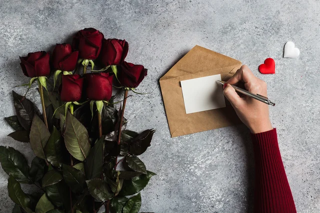Woman holding pen in hand writing a love letter with a greeting card on Valentine's Day.