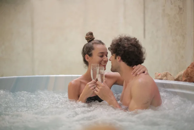 A couple enjoying a relaxing time in a hot tub, holding glasses and cherishing the moment of tranquility.