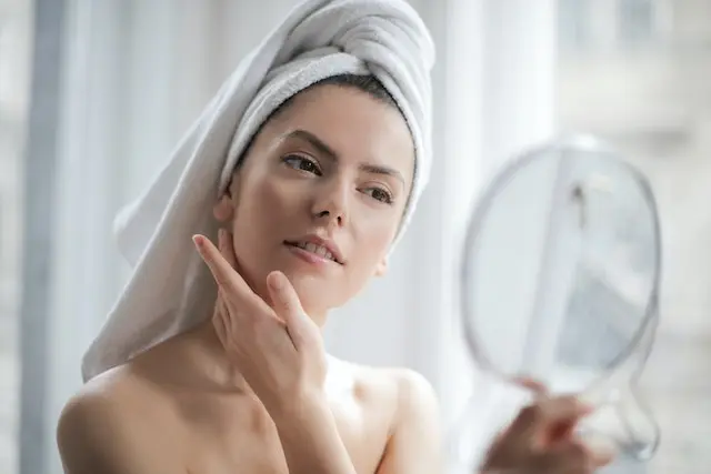 photo of woman with a towel on head looking in the mirror