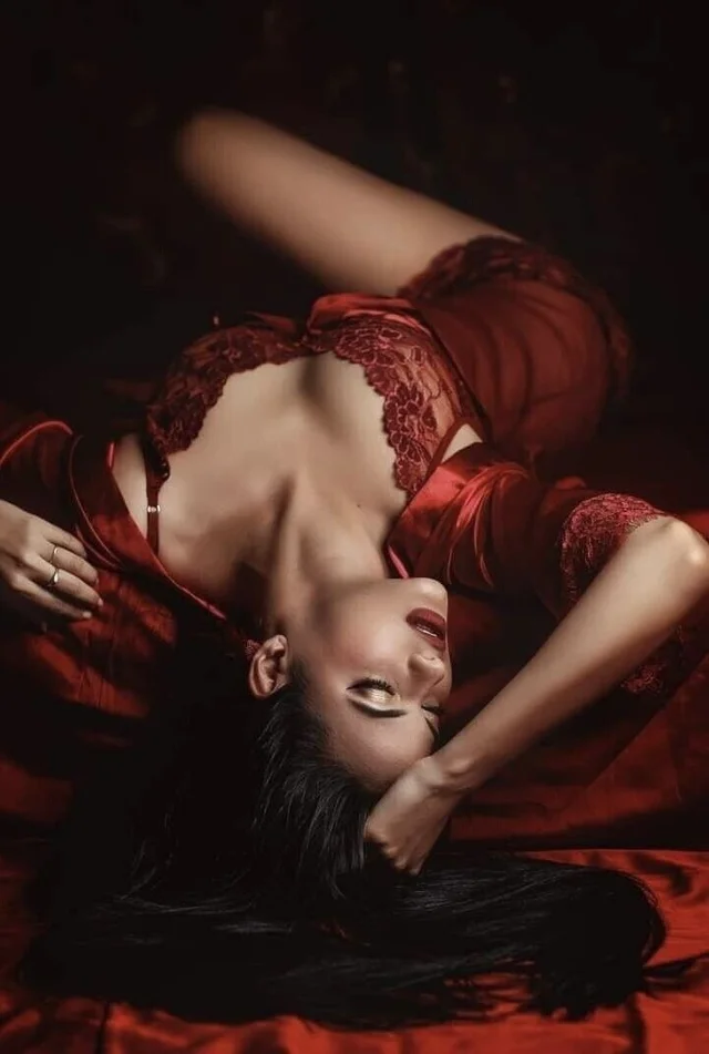 A woman in red lingerie seductively poses on a bed, exuding allure and confidence.