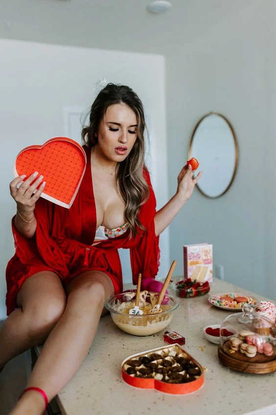 A model in a red robe sits on a table, holding a heart-shaped box. Perfect for Valentine's Day photoshoot ideas.