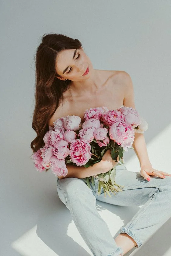 A woman sitting on a white floor, gracefully holding a bouquet of delicate pink flowers.