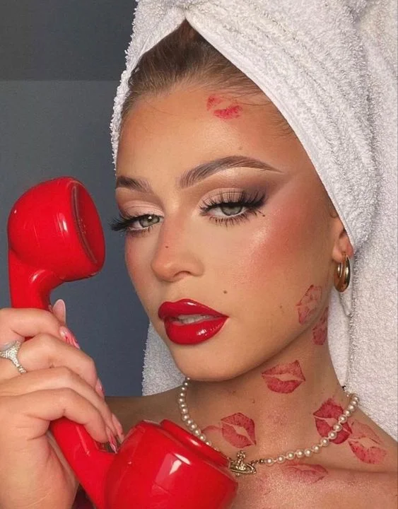 A woman with red lipstick on her face holding a red telephone.