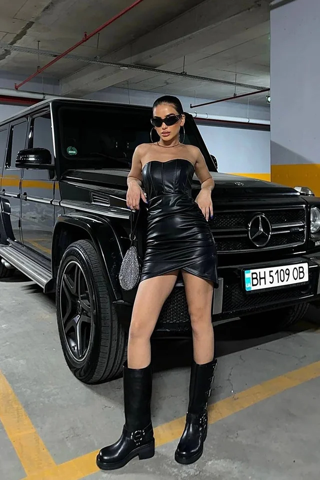 A woman in a Strapless Black Mini Leather Dress striking a pose next to a sleek black car.