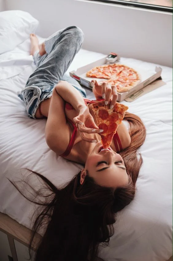 A woman enjoying pizza while lying on a bed.