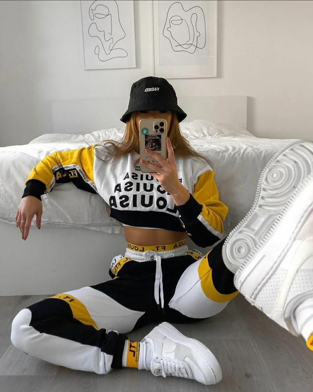 A woman in a yellow and black joggers sitting on the floor.