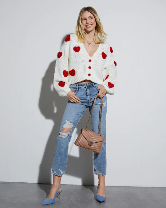 A woman wearing ripped jeans and a heart-shaped knit cardigan.