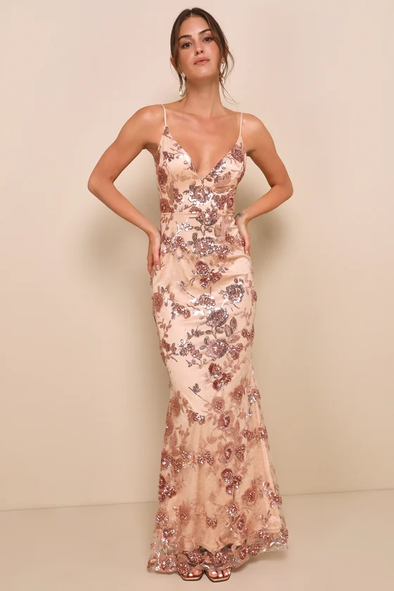 A woman modeling an elegant blush pink prom dress with a plunging v-neckline and allover floral sequin embroidery in a figure-hugging mermaid silhouette.
