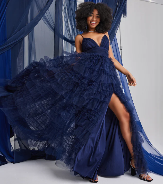 A smiling woman in a stunning navy blue tulle ball gown with a sweetheart neckline, layered ruffled skirt, and daring high front slit, perfect for making a glamorous prom entrance.