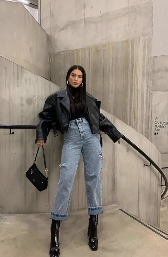 a woman standing on stairs wearing leather jacket, denim jeans, and boots